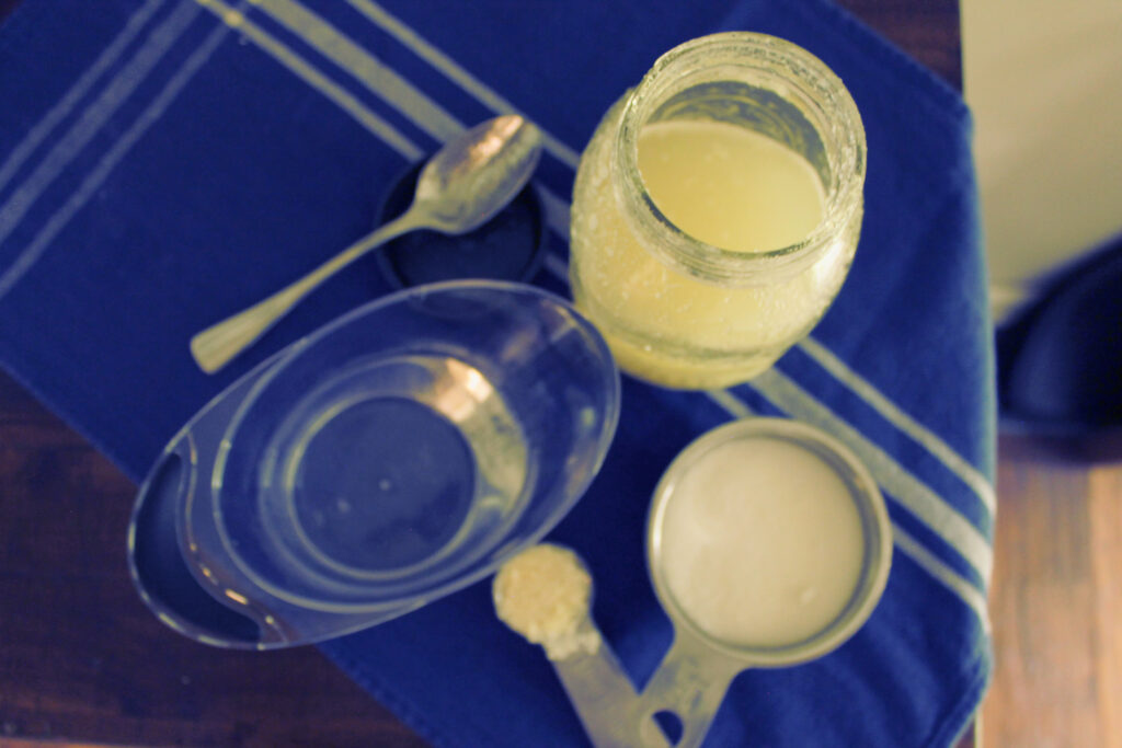 cup of water, spoon, tablespoon with potato flakes, sugar, potato flake starter on top of blue tea towel