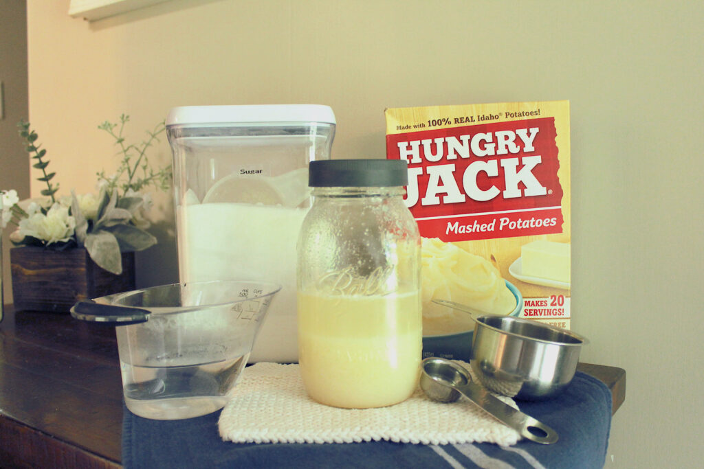 sugar, potato flakes, cup of water, measuring cups, potato flake starter sitting on dish cloth