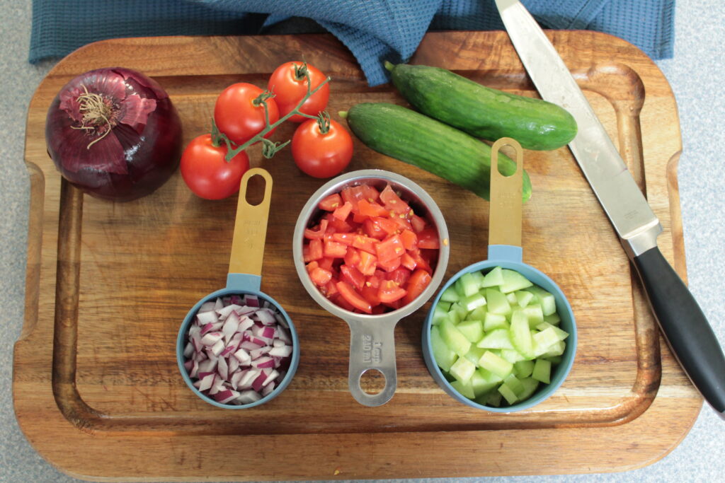 red onion, tomatoes, cucumbers on cutting board with knife