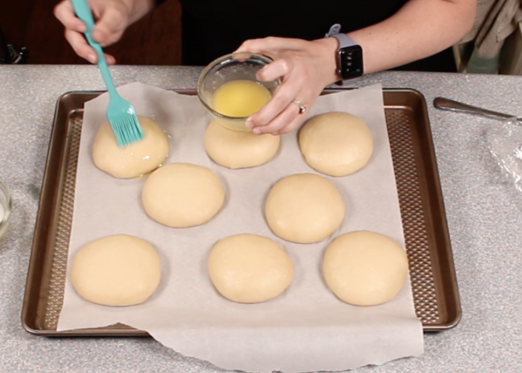 basting risen bun dough with butter on top of parchment paper