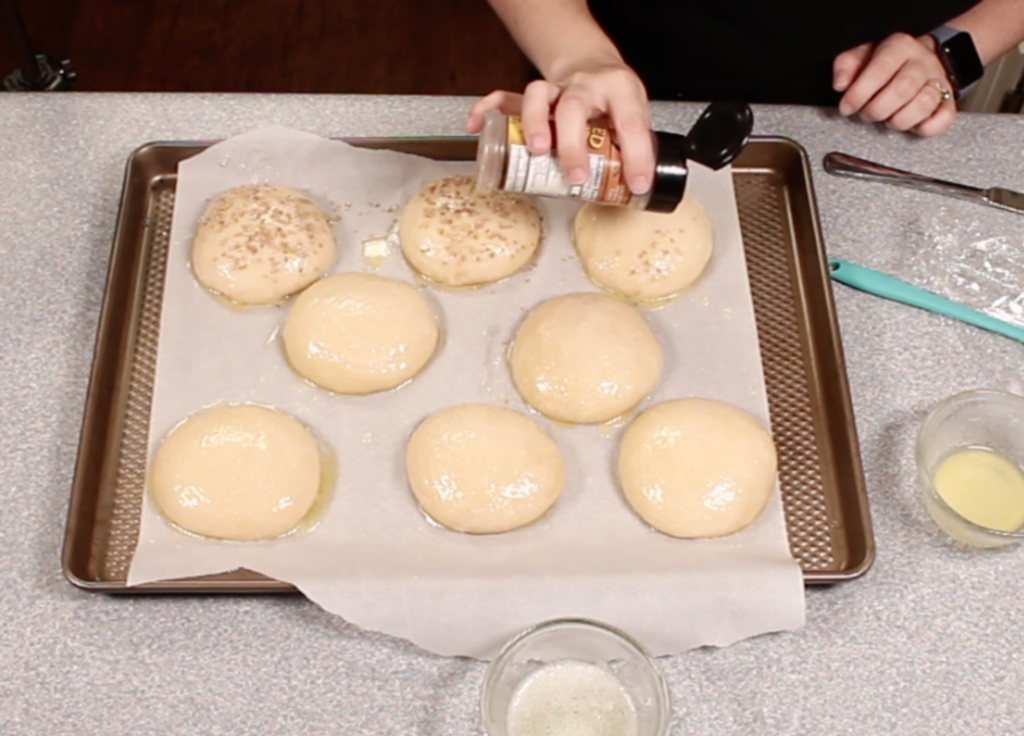 Sprinkling sesame seeds on top of risen basted bun dough