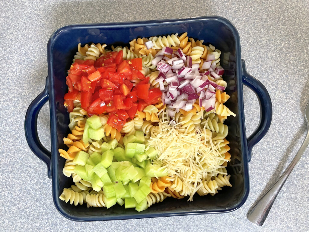 pasta salad in blue dish topped with onion, tomatoes, and cucumber