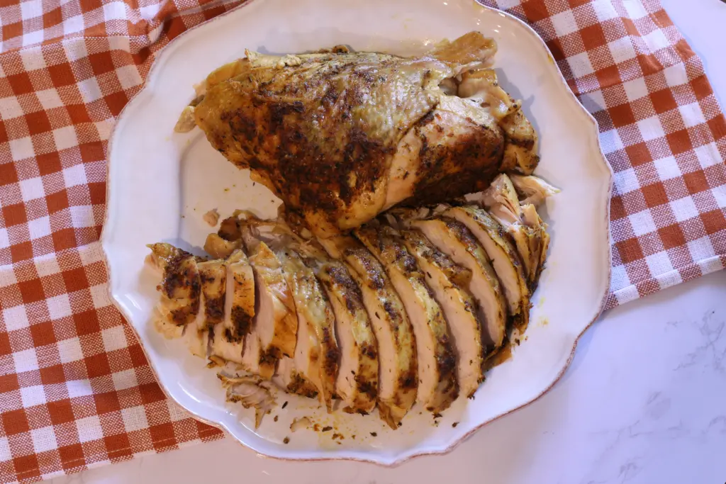 two removed turkey breast on a plate, one whole, one sliced