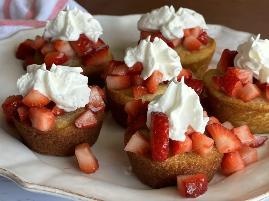 six sourdough strawberry shortcakes topped with strawberries and whipped topping on a white plate