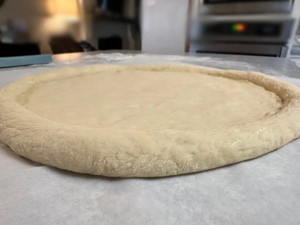 stretched pizza dough with crust left thicker