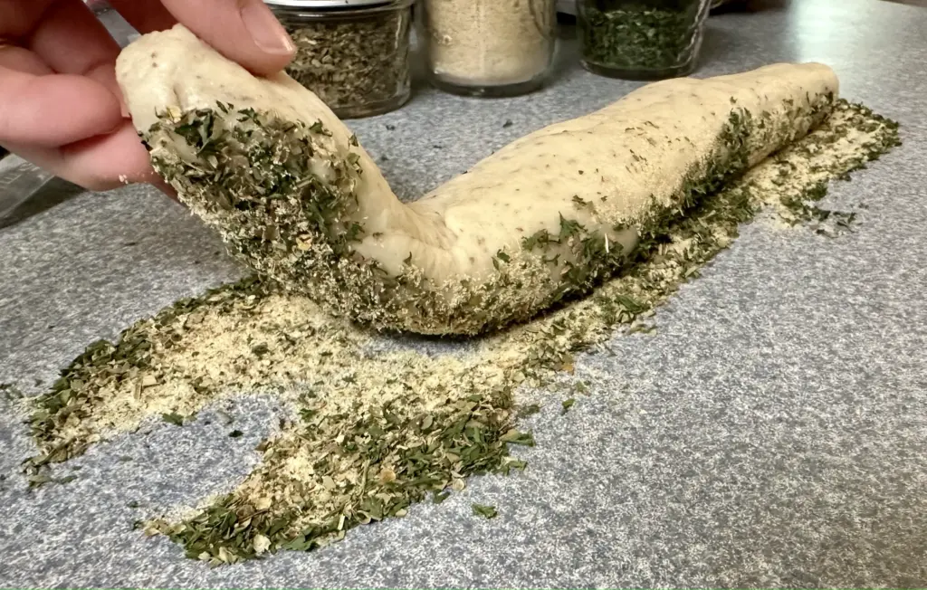 dredging potato flake sourdough garlic herb and cheese bread in the Italian herb blend