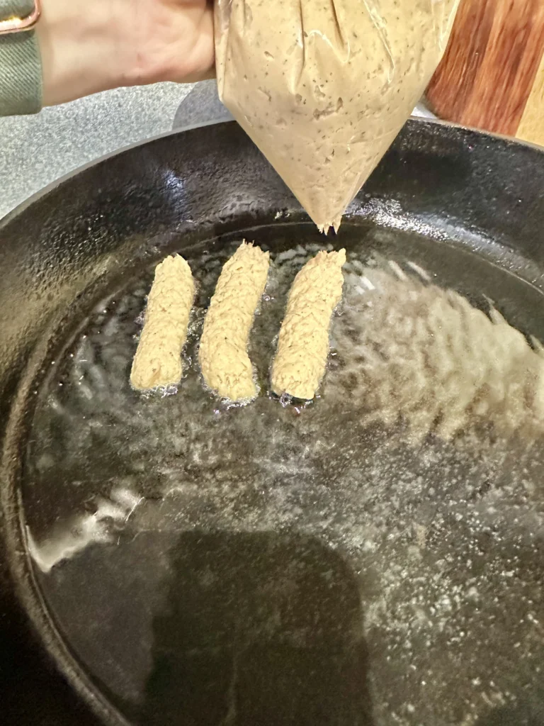 piping salmon fish sticks into hot coconut oil in cast iron skillet