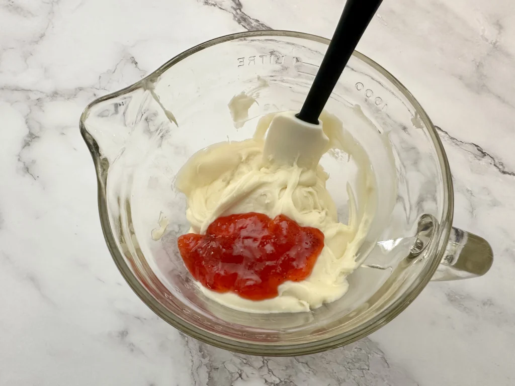 adding strawberry jam to cream cheese icing